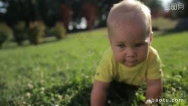 在夏季公园的特写里，快乐的金发婴儿蓝眼睛在绿色的草地上爬行